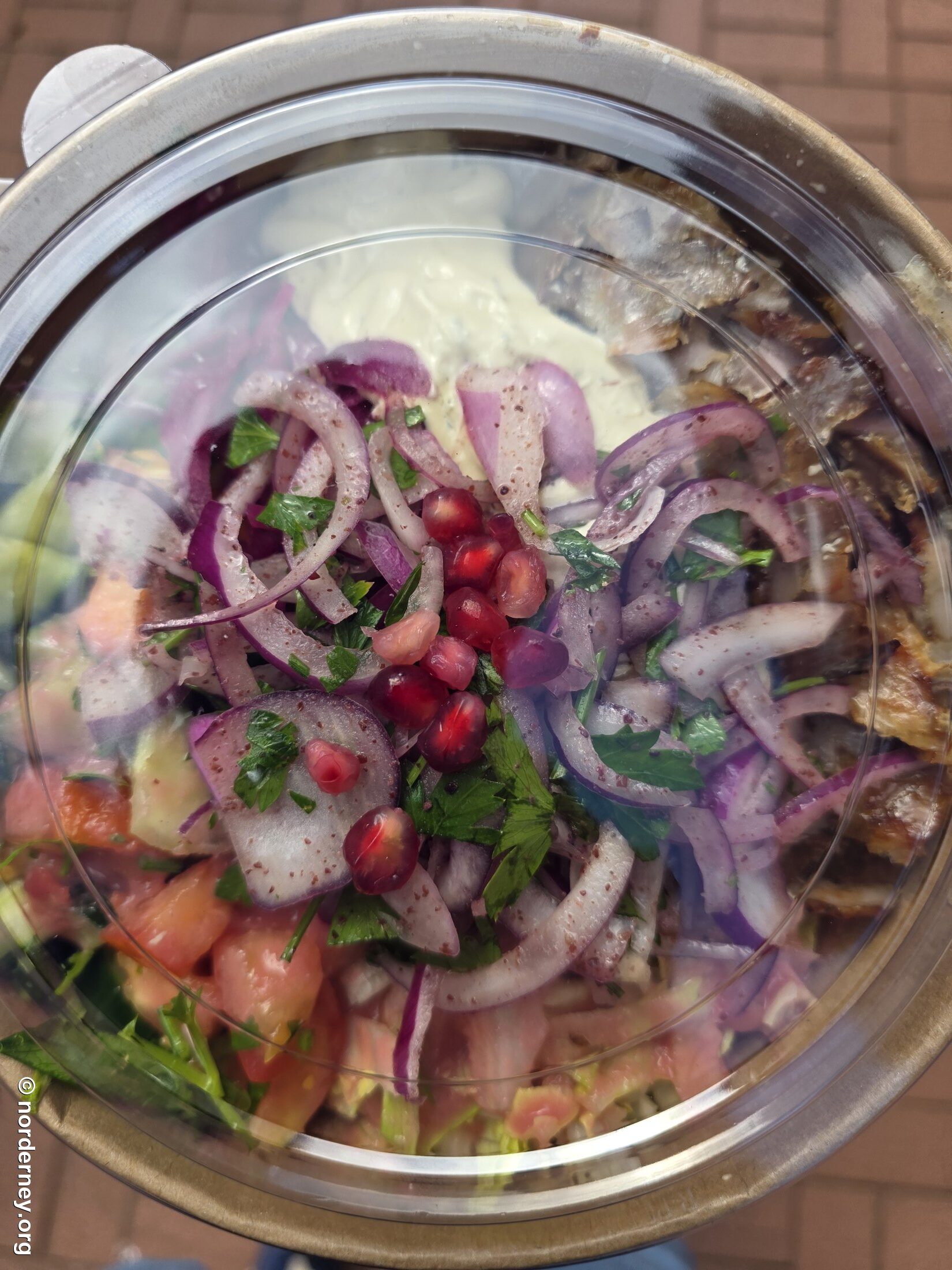 Döner-Portion in einer transparenten Schale bei Dönerey Norderney, mit rotem Zwiebelsalat, Granatapfelkernen, Petersilie, Tomatenstücken und Joghurt-Knoblauch-Sauce