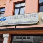 El Greco Norderney: Griechische Spezialitäten in der Jann-Berghaus-Straße El Greco Norderney – Schild „Griechische Spezialitäten“ in der Jann-Berghaus-Straße