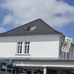 Café Extrablatt Norderney: Frühstücksbuffet, Cocktails und Terrasse am Kurplatz Café Extrablatt Norderney – Giebel mit Ausleger-Fahne „CAFE Extrablatt – Das Genuss Extra“ und verglastem Wintergarten-Anbau am Kurplatz