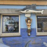 Haifischbar Norderney: Kneipe mit Live-Musik und Sky Sport Fassade der Haifischbar Norderney mit hölzernem Schwertfisch, geschnitzter Galionsfigur und Bitburger-Leuchtschild