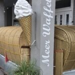 Meer Waffel Norderney: Waffeln, Crêpes & Softeis in der Poststraße Meer Waffel Norderney – Schild mit Softeis-Figur in der Poststraße