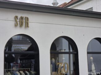 SØR Norderney – Fassade am Kurplatz mit goldenem Schriftzug, drei Rundbogenfenstern und Jubiläums-Dekoration „70 Jahre“ im Schaufenster