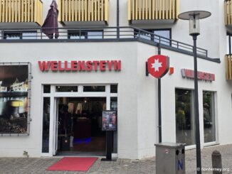 Wellensteyn-Store auf Norderney – Fassade in der Adolfsreihe mit rotem Schriftzug-Logo, weiß-rotem Wappen und rotem Teppich am Eingang