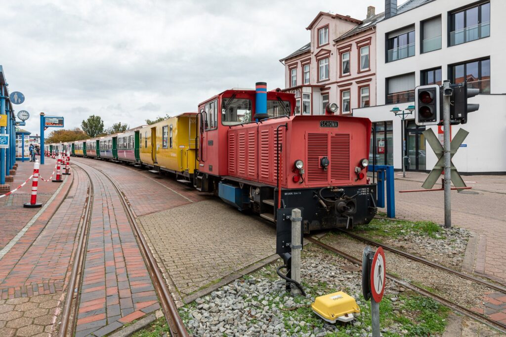 Zug der Borkumer Kleinbahn mit roter Diesellok und bunten Wagen am Bahnhof Borkum