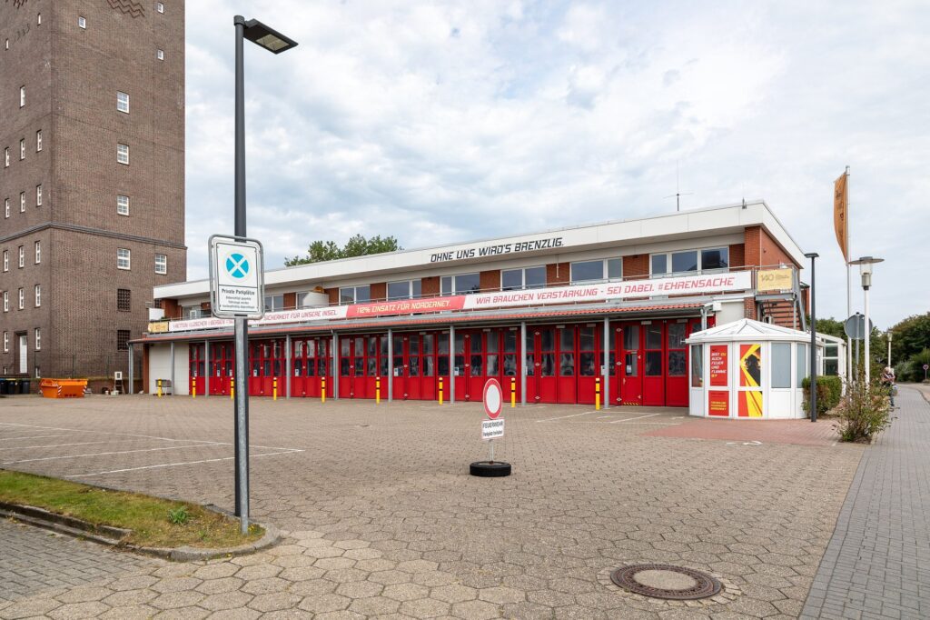 Feuerwache der Freiwilligen Feuerwehr Norderney mit roten Fahrzeugtoren an einem bewölkten Tag