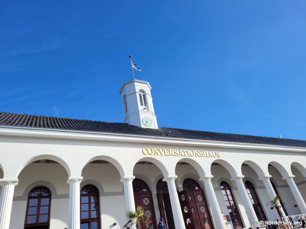 Säulengang des Conversationshauses auf Norderney mit goldenem Schriftzug und Uhrenturm