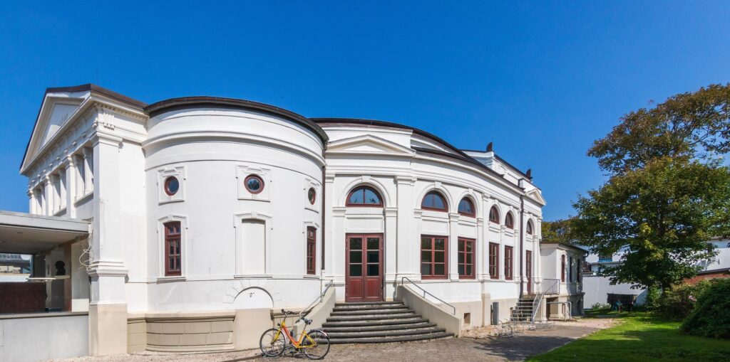 Seitenfront des denkmalgeschützten Kurtheaters Norderney mit Rundbogenfenstern und Treppenaufgang