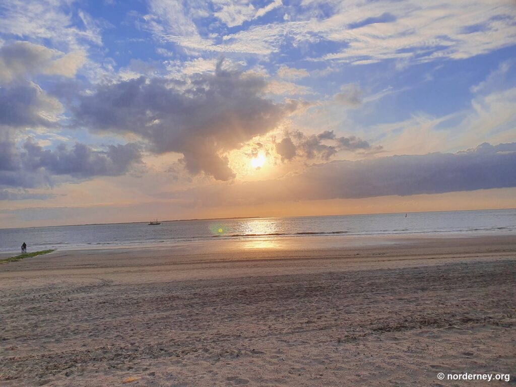 Tief stehende Abendsonne bricht durch Wolken über dem Strand von Norderney