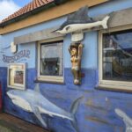 Kneipen Norderney: Bars, Disco und Nachtleben im Überblick Blaue Fassade der Haifischbar auf Norderney mit Hai-Wandbild, Schwertfisch und Galionsfigur