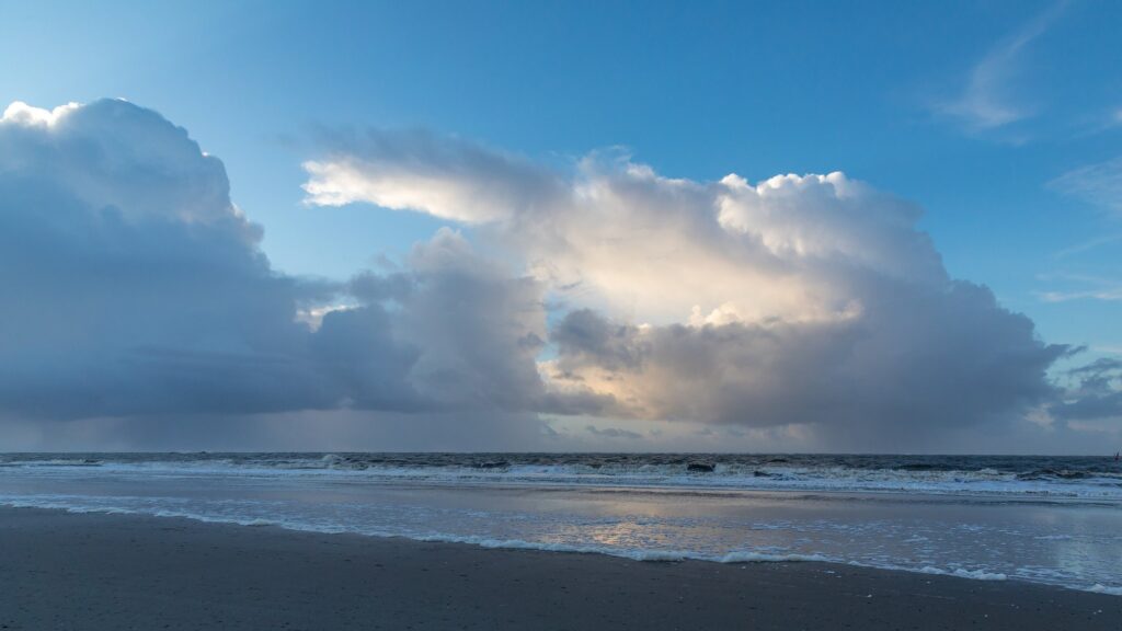 Dunkle Schauerwolken und schäumende Brandung am Weststrand von Norderney