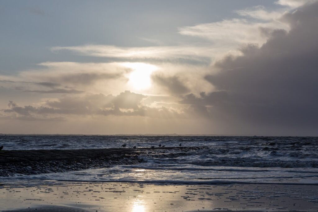 Dunkle Wolken und aufgewühlte Brandung an einer Buhne am Weststrand von Norderney