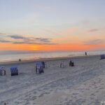 Norderney im Oktober: Wetter, Zugvögel und Herbstferien Blau-weiße Strandkörbe am Strand von Norderney bei Sonnenuntergang über der Nordsee