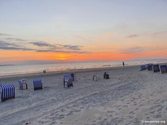 Blau-weiße Strandkörbe am Strand von Norderney bei Sonnenuntergang über der Nordsee