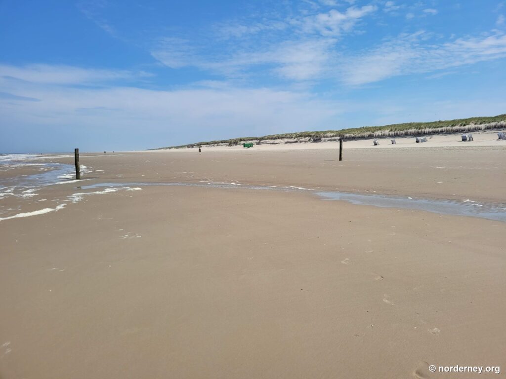 Weiter, fast menschenleerer Sandstrand auf Norderney mit Dünenkette und vereinzelten Strandkörben