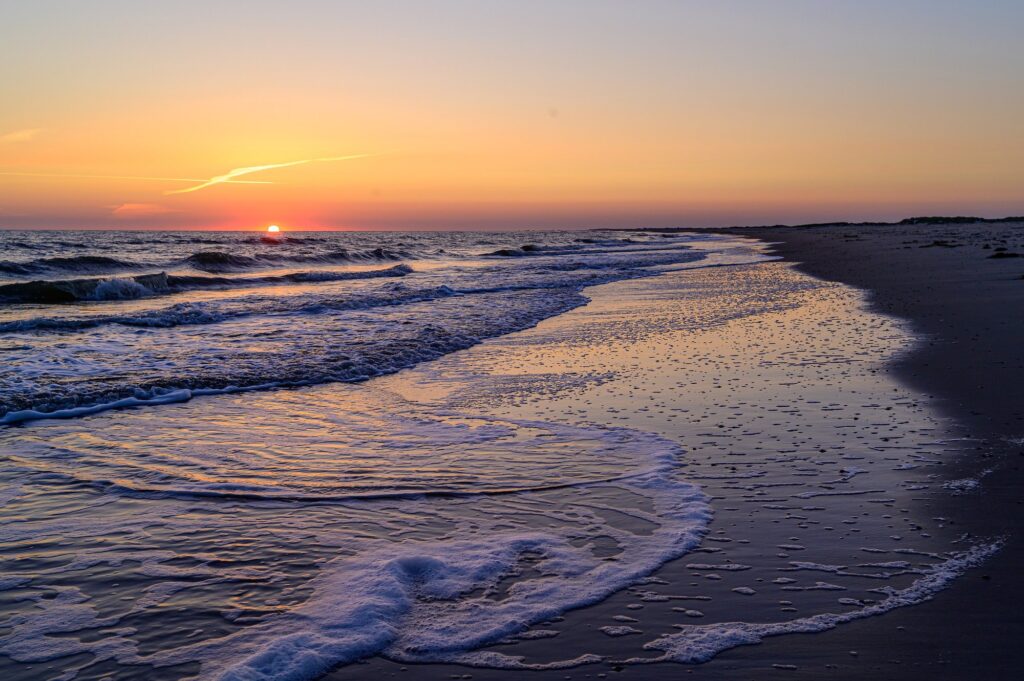 Sonnenaufgang über der Nordsee mit auflaufenden Wellen am Strand von Norderney