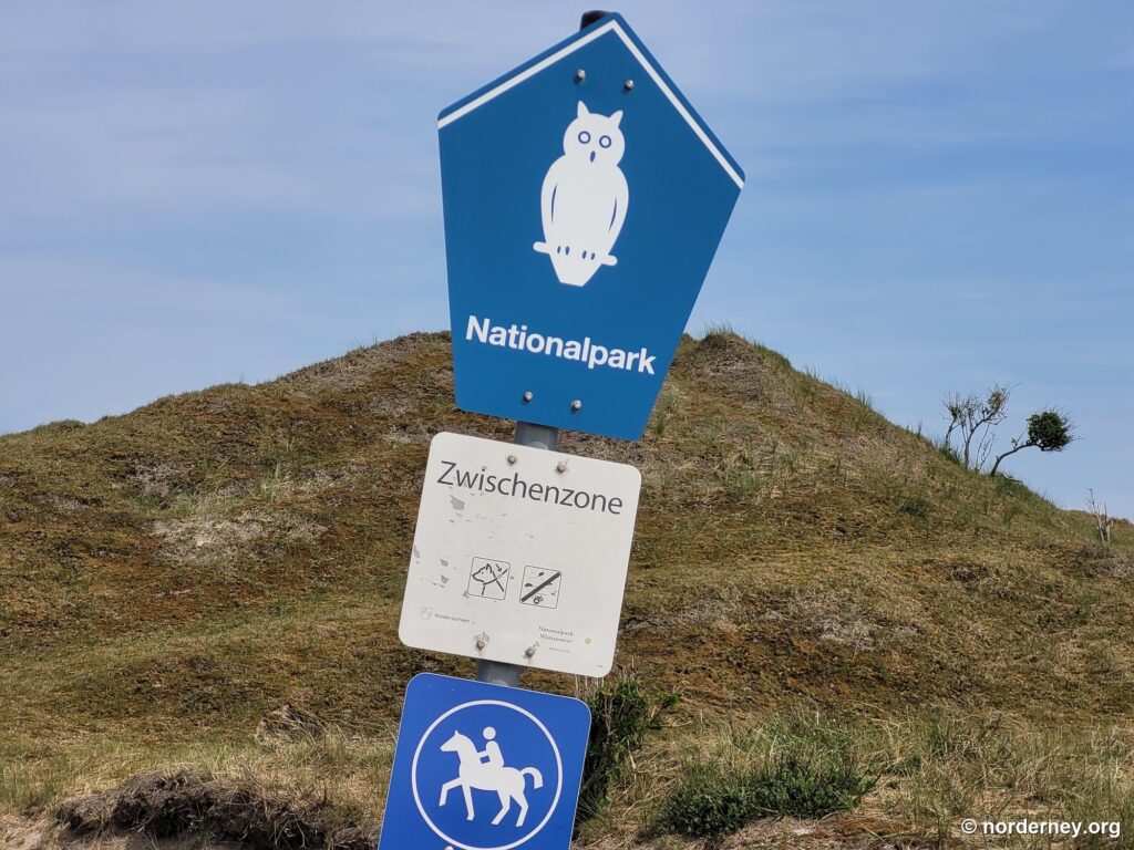 Nationalpark-Schild mit Eule und Hinweis Zwischenzone vor einer Düne auf Norderney