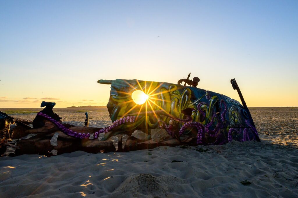 Rostiges, mit Kraken-Graffiti bemaltes Schiffswrack im Sand am Ostende von Norderney