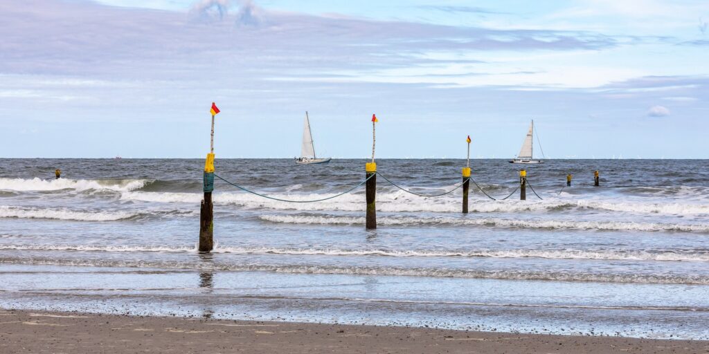 Pfähle mit rot-gelben Fahnen und Leine markieren den Badebereich am Strand von Norderney