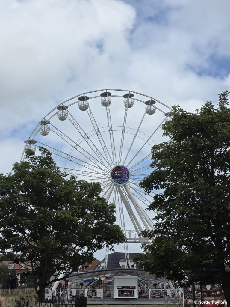 Weißes Riesenrad zwischen Laubbäumen im Ortskern von Norderney an einem Sommertag