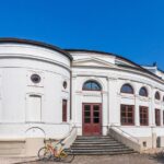 Wochenmarkt Norderney: Zeiten, Standort und Angebot Seitenansicht des weißen Kurtheaters von Norderney mit Freitreppe unter blauem Himmel