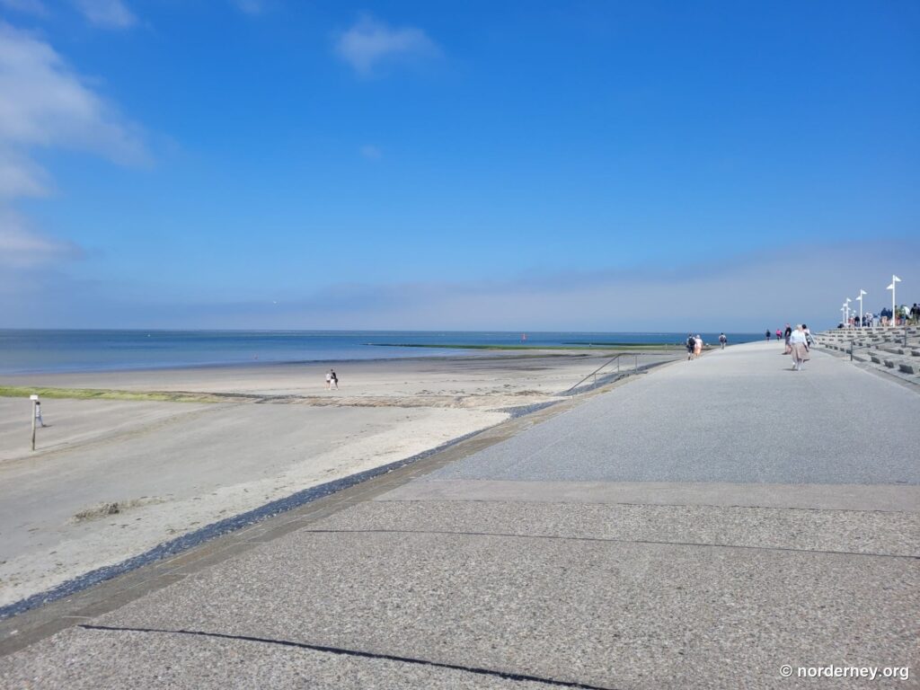 Breite Strandpromenade von Norderney mit weißen Fahnenmasten und Strand bei Ebbe